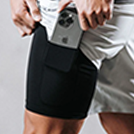 Person inserting a smartphone into the pocket of black athletic shorts.